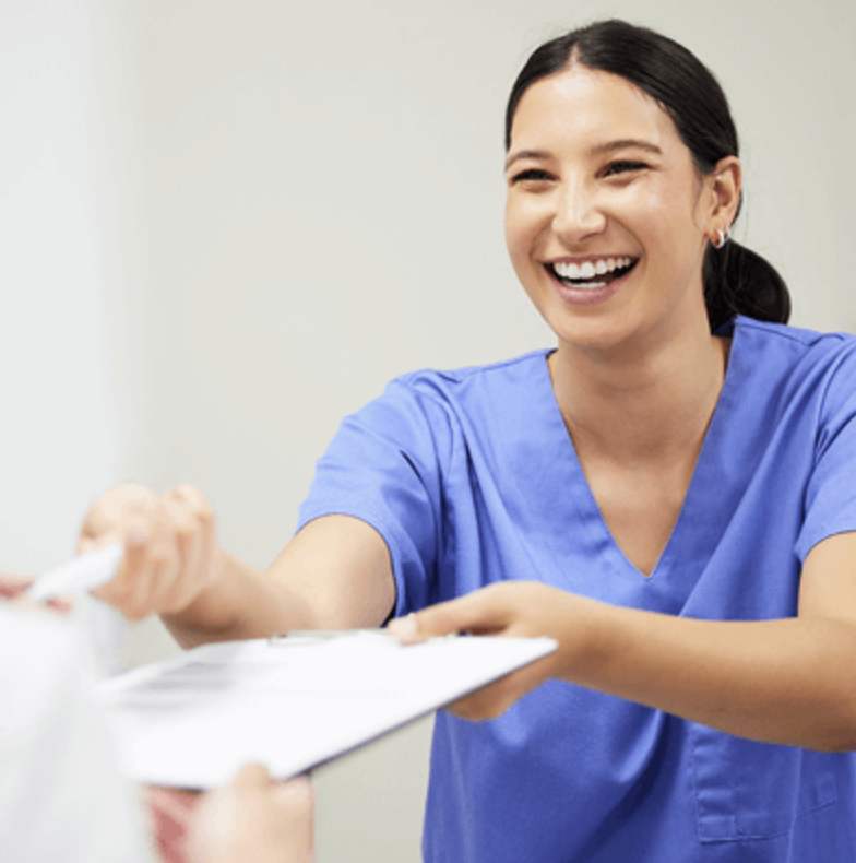 Young woman smiling wearing blue scrubs and handing over clipboard